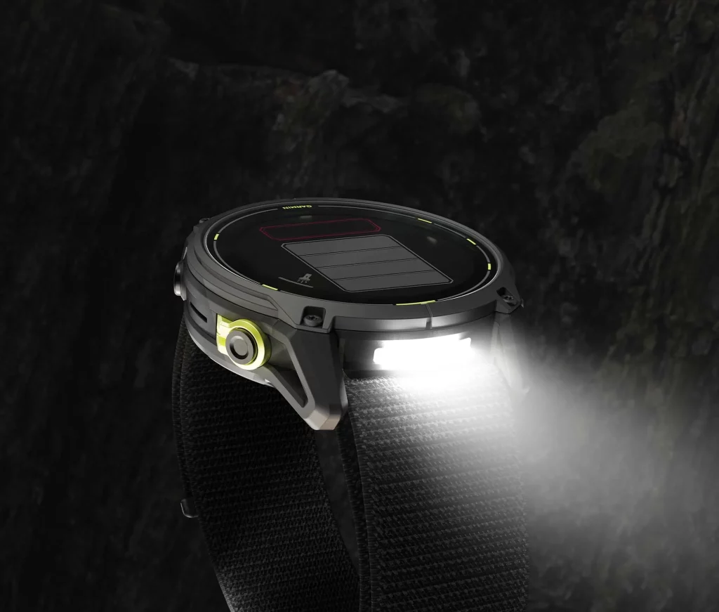 Rugged smartwatch with solar panel and built-in flashlight against a dark rocky backdrop